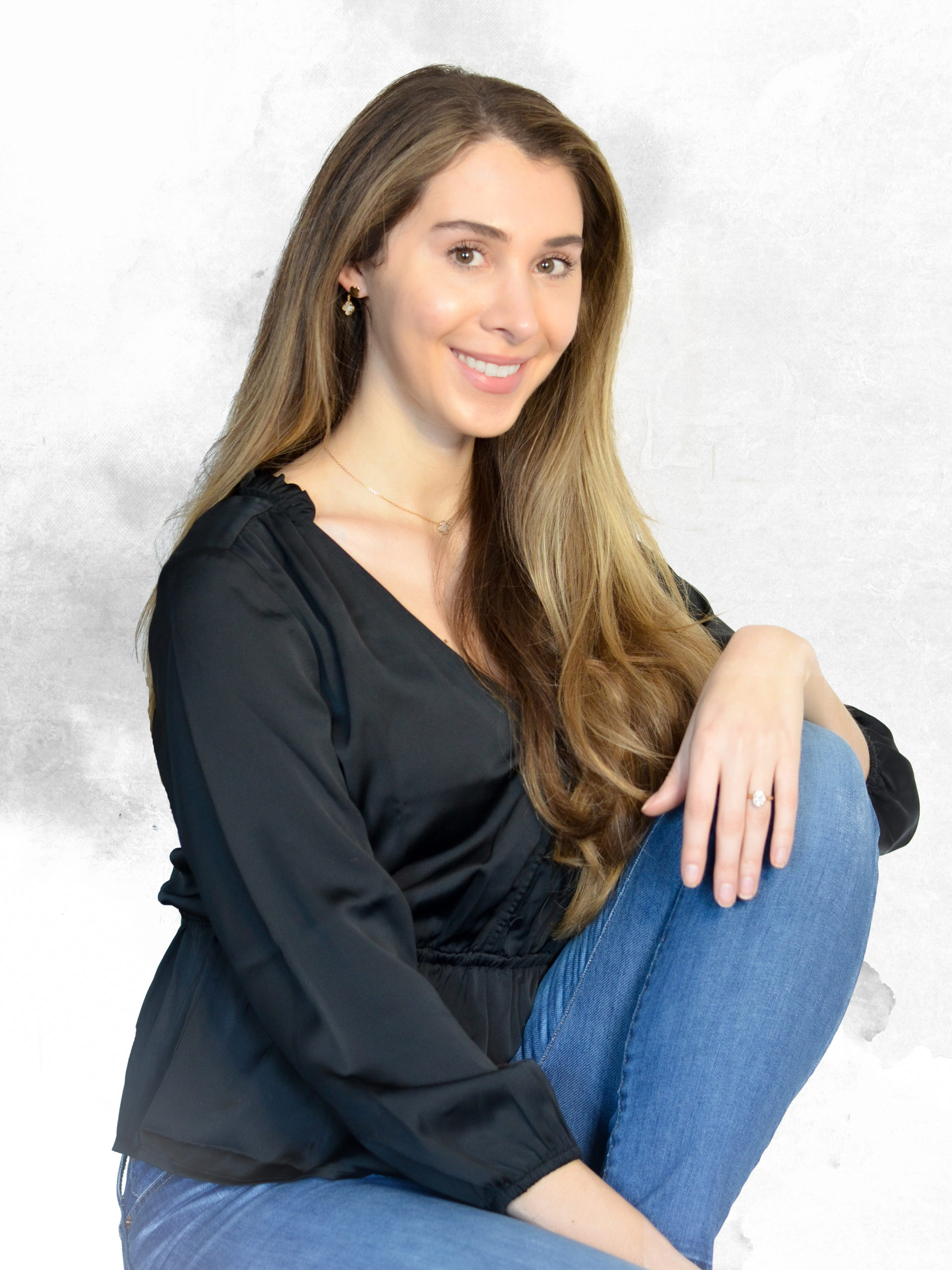 This is an image of a girl with brown hair sitting with her knee up for a headshot photo.